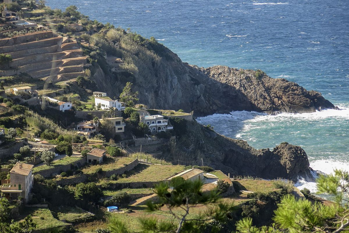 Stone terraced slopes and a few houses lead down to a rocky headland and the blue sea on the Serra de Tramuntana coast near Banyalbufar.