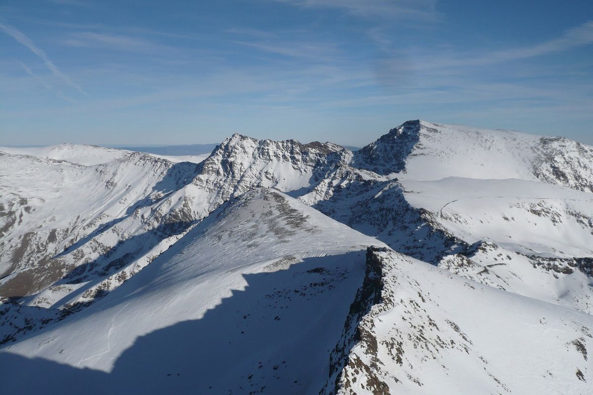 Snow covered ridges and peaks of the Sierra Nevada, including the dome of Mulhacen, rise under a pale blue sky.